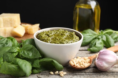 Photo of Tasty pesto sauce in bowl, pine nuts, garlic and basil on wooden table
