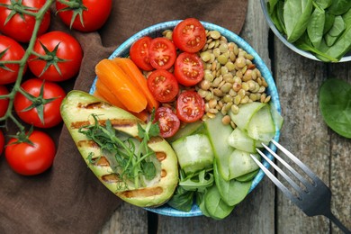 Photo of Delicious lentil bowl with avocado, tomatoes, carrot and cucumber on wooden table, flat lay