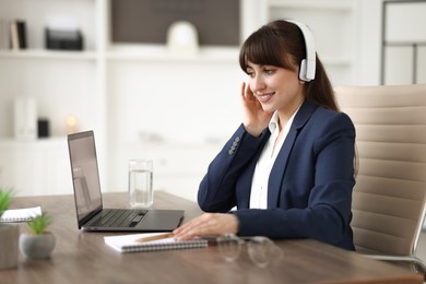 Photo of Woman in headphones watching webinar at wooden table in office