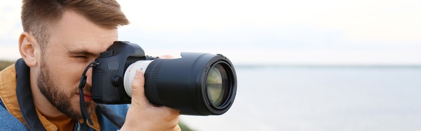 Image of Male photographer taking picture with professional camera outdoors, space for text. Banner design