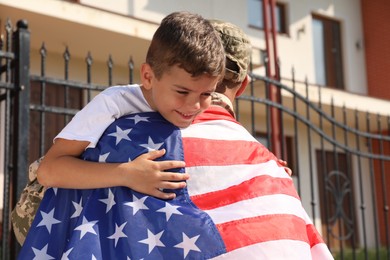 Photo of Soldier with flag of USA and his little son hugging outdoors