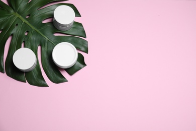 Photo of Tropical leaf and jars of cream on pink background, flat lay. Space for text