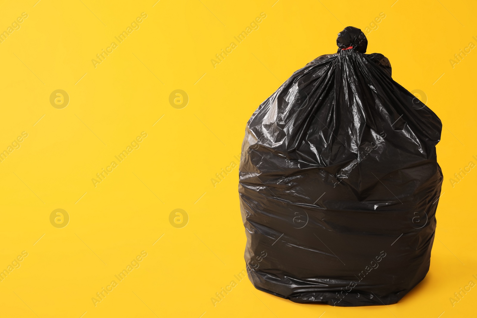 Photo of Trash bag full of garbage on yellow background. Space for text