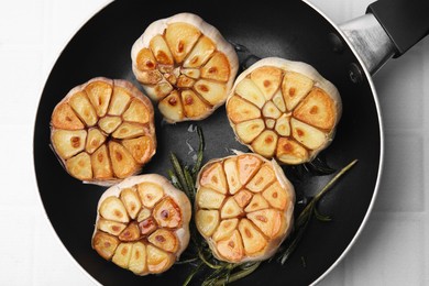 Photo of Frying pan with fried garlic and rosemary on white table, top view