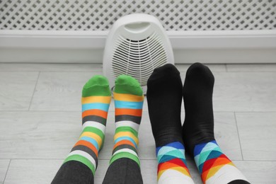 Photo of Couple warming feet near modern heater indoors, closeup