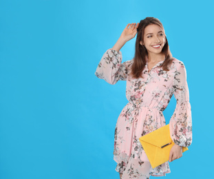 Photo of Young woman wearing floral print dress with elegant clutch on light blue background