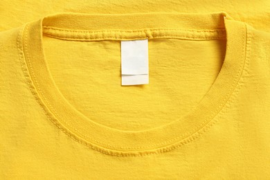 Photo of Blank clothing label on yellow T-shirt, top view