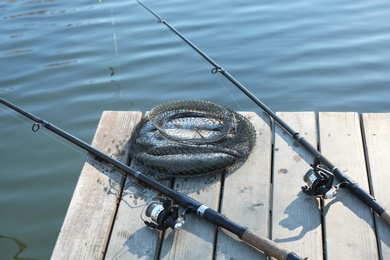 Photo of Fishing rods and fresh fish on wooden pier near pond