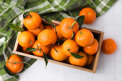 Photo of Wooden crate with fresh ripe tangerines and leaves on white tiled table, flat lay