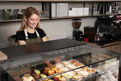 Photo of Happy seller taking delicious dessert from showcase in bakery shop