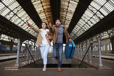 Photo of Being late. Worried couple with suitcase running at train station