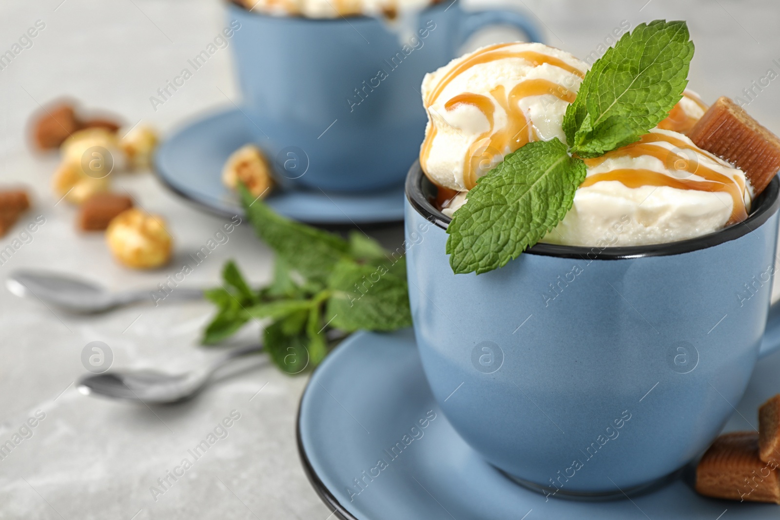 Photo of Cup of delicious ice cream with caramel sauce, candies and mint on grey table, closeup