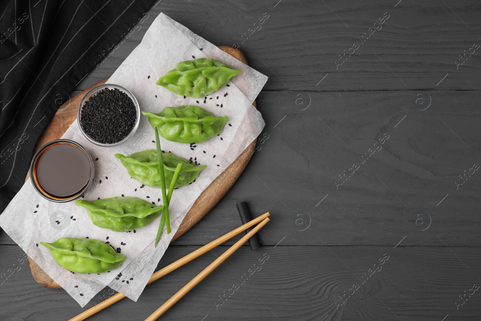 Photo of Delicious green dumplings (gyozas) served on grey wooden table, flat lay. Space for text