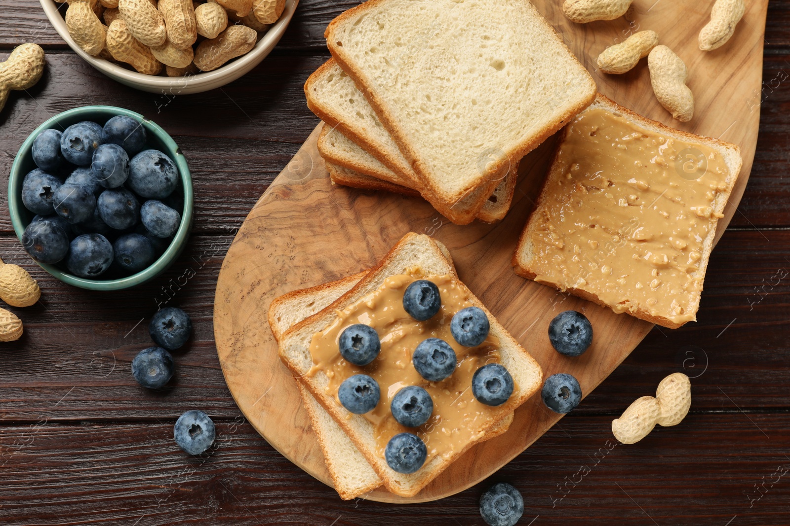 Photo of Delicious toasts with peanut butter, blueberries and nuts on wooden table, flat lay