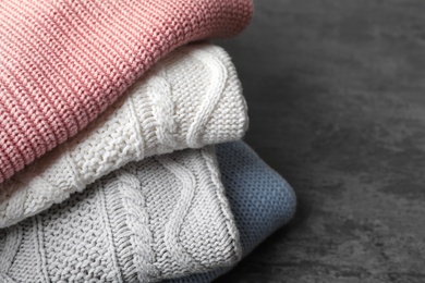 Photo of Stack of folded knitted sweaters on table, closeup. Space for text