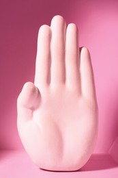 One hand sculpture on pink background, closeup
