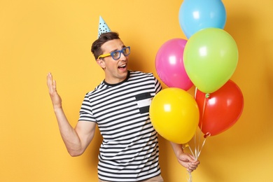 Photo of Young man with bright balloons on color background. Birthday celebration
