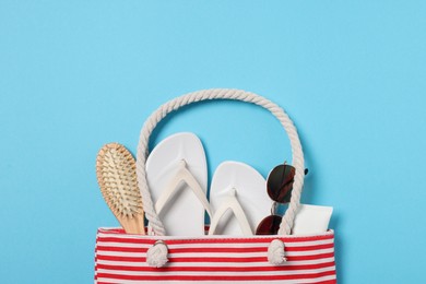 Flat lay composition with bag and other beach accessories on light blue background. Space for text