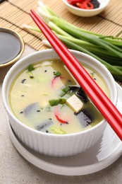 Bowl of delicious miso soup with tofu and chopsticks served on light grey table, closeup