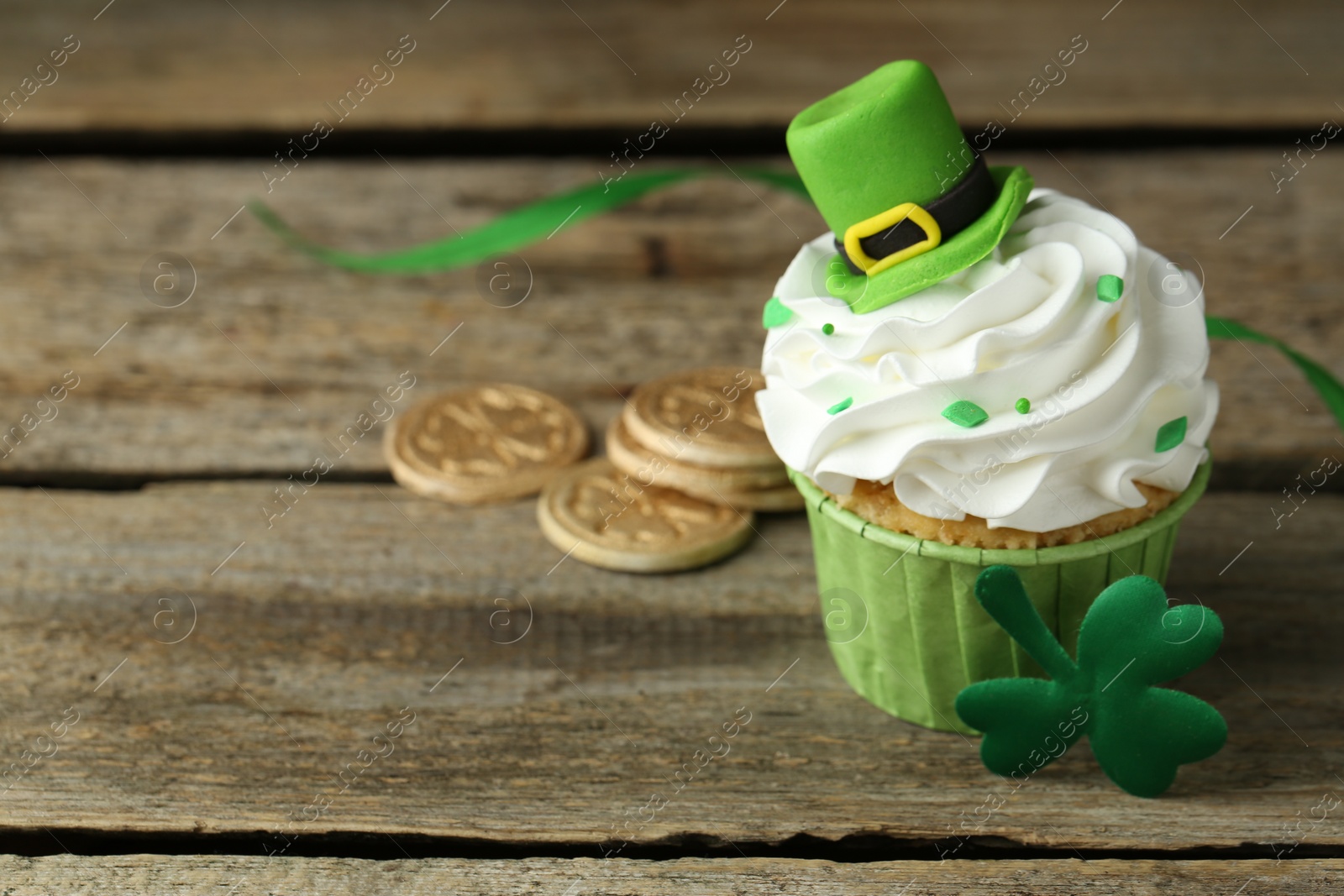 Photo of St. Patrick's day party. Tasty cupcake with green leprechaun hat topper on wooden table, closeup. Space for text