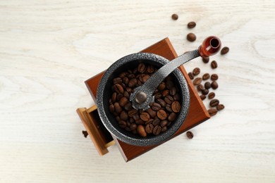 Photo of Vintage manual coffee grinder with beans on white wooden table, top view