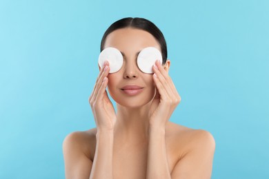 Photo of Beautiful woman removing makeup with cotton pads on light blue background