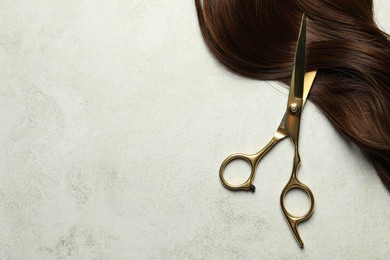 Photo of Professional hairdresser scissors with brown hair strand on grey table, top view. Space for text