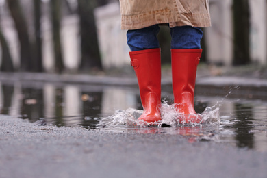 Photo of Woman in rubber boots jumping over puddle on rainy day, closeup. Space for text