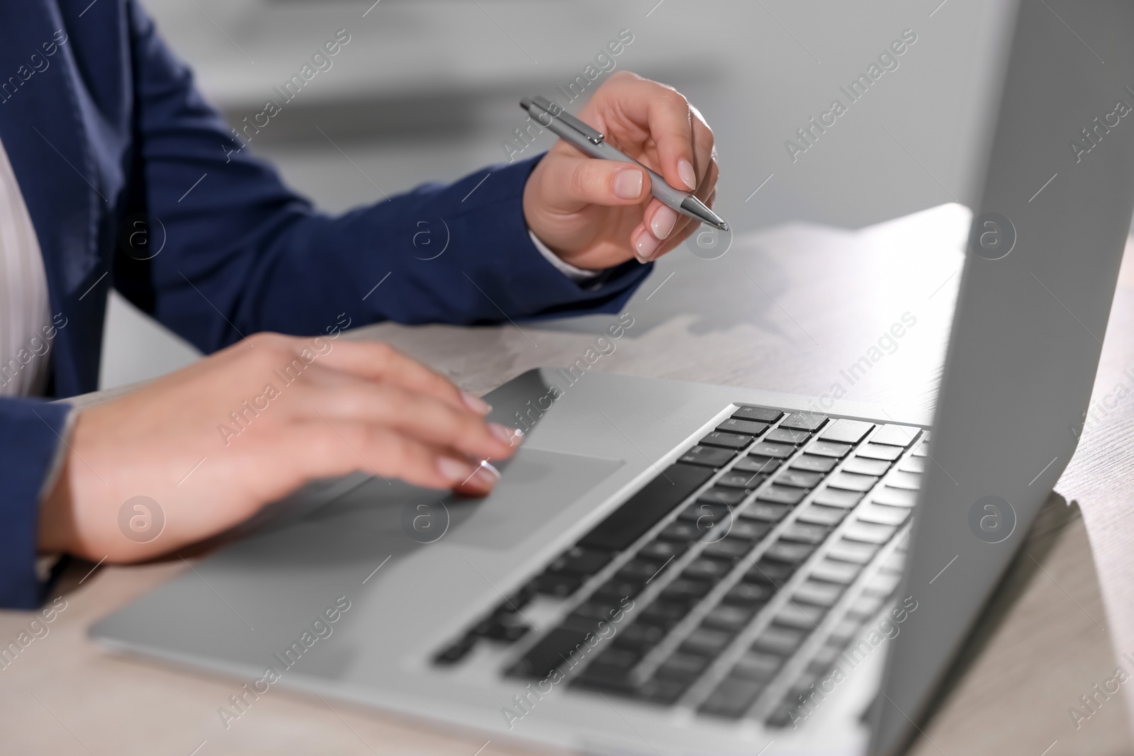 Photo of Woman with pen working on laptop at wooden table, closeup. Electronic document management