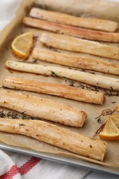 Baking tray with cooked salsify roots, lemon and thyme on table, closeup
