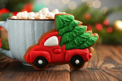 Photo of Tasty Christmas cookie in shape of car with fir tree and cocoa with marshmallows on wooden table, closeup. Space for text