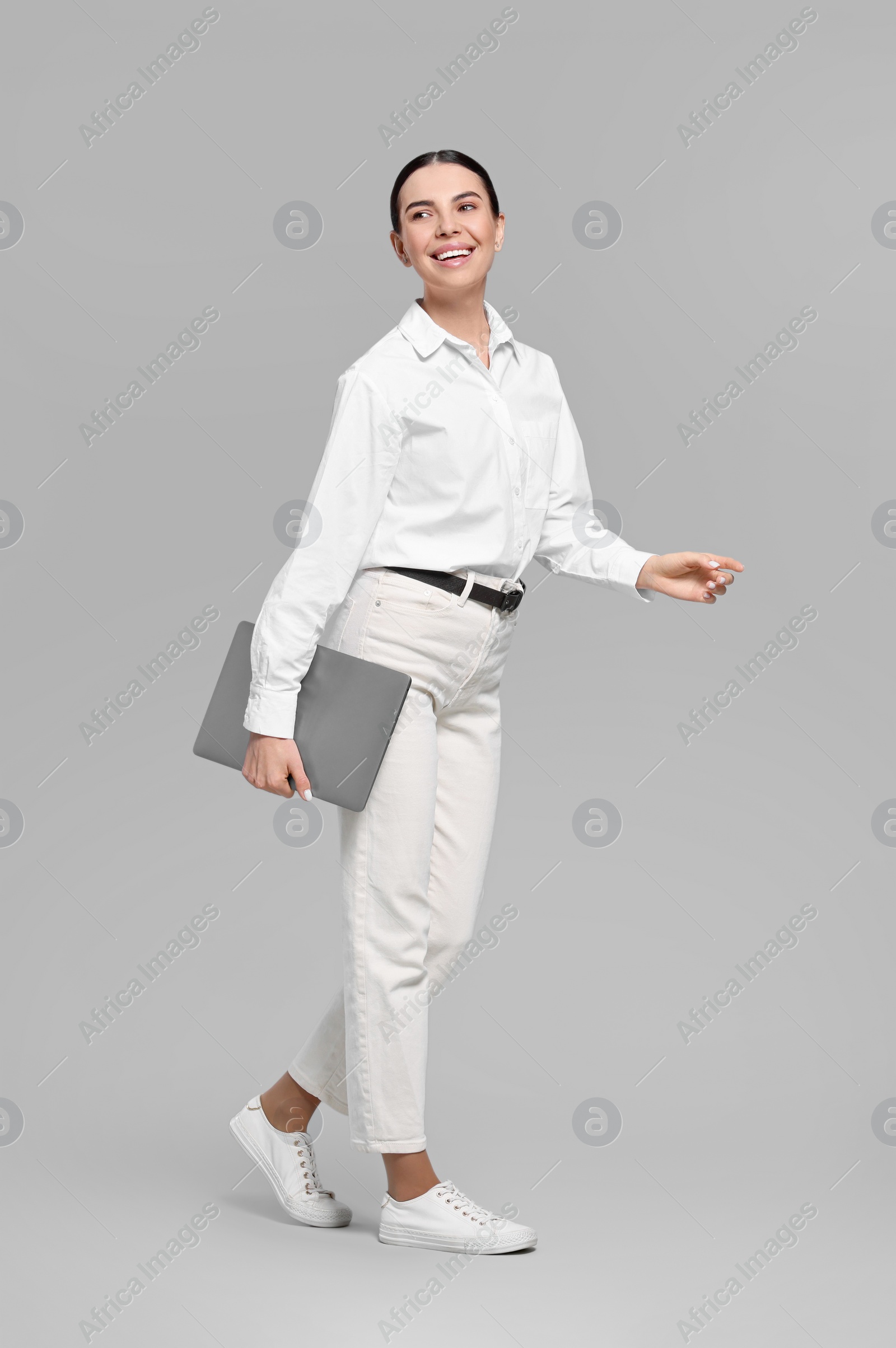 Photo of Happy woman with laptop walking on light gray background