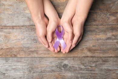 Photo of Man and woman holding purple awareness ribbon on wooden background, top view