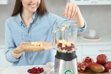 Photo of Woman adding mango into blender with ingredients for smoothie in kitchen, closeup