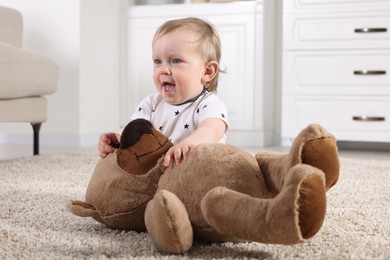 Photo of Cute little child with teddy bear on carpet at home