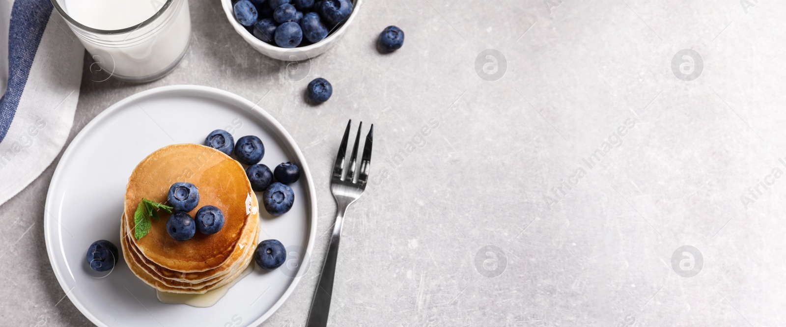 Image of Plate of tasty pancakes with blueberries and honey on light grey table, flat lay with space for text. Banner design