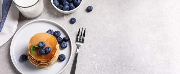 Plate of tasty pancakes with blueberries and honey on light grey table, flat lay with space for text. Banner design