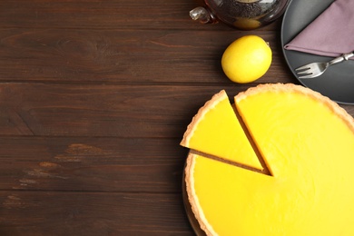 Photo of Delicious homemade lemon pie and tea on wooden table, flat lay. Space for text