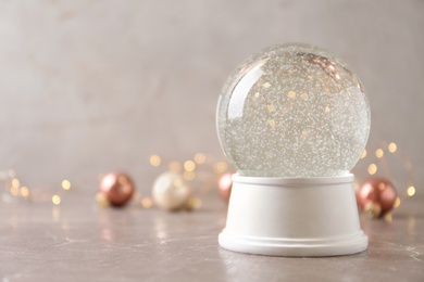 Photo of Snow globe and Christmas decorations on marble table against festive lights, space for text