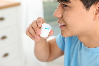 Man holding cap with mouthwash, closeup view. Teeth care