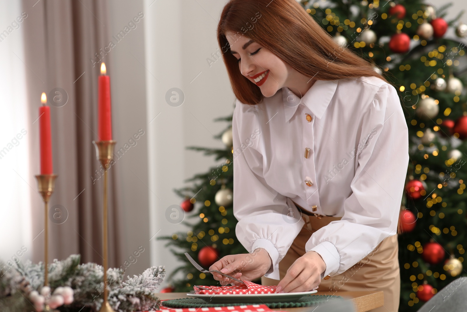 Photo of Beautiful young woman setting table near Christmas tree at home, space for text