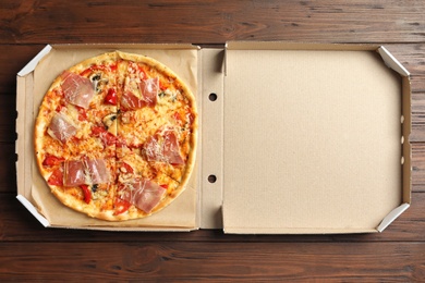 Photo of Carton box with delicious pizza on wooden background, top view