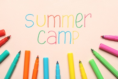 Photo of Text SUMMER CAMP and colorful felt tip pens on color background, flat lay
