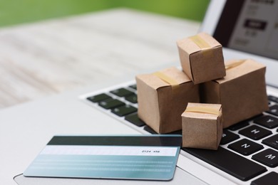 Photo of Internet shopping. Small cardboard boxes, credit card and laptop on light wooden table, closeup. Space for text