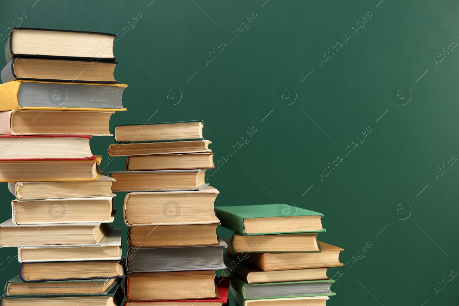 Photo of Many hardcover books near green chalkboard, space for text. Library material