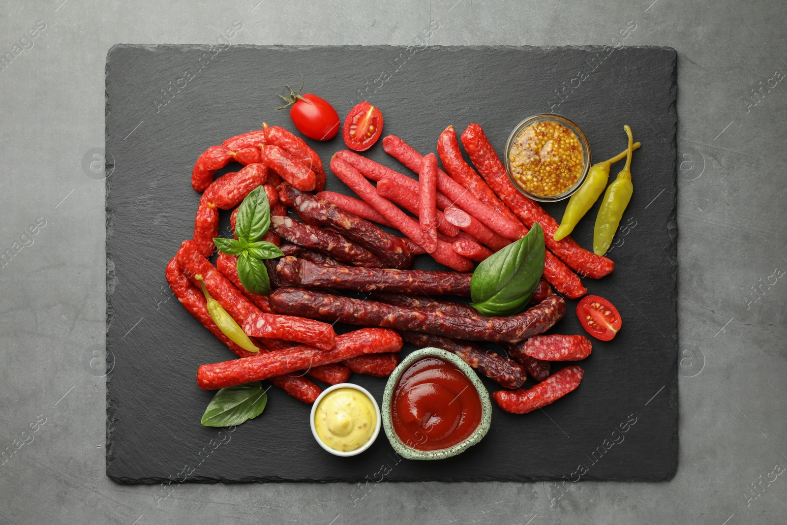 Photo of Different thin dry smoked sausages and sauces on grey table, top view