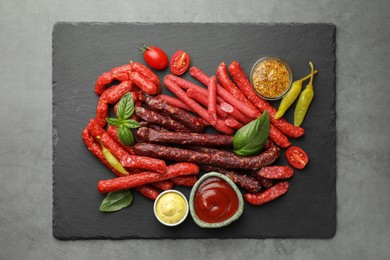 Photo of Different thin dry smoked sausages and sauces on grey table, top view