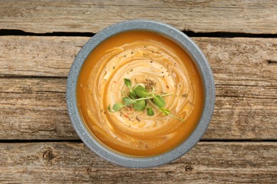 Photo of Delicious pumpkin soup with microgreens in bowl on wooden table, top view