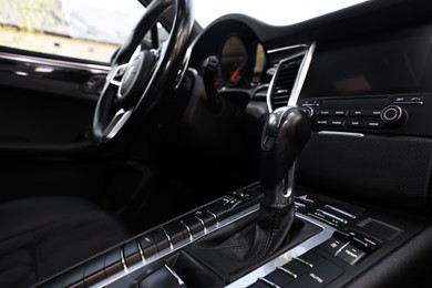 Gear stick and steering wheel inside of modern black car, closeup