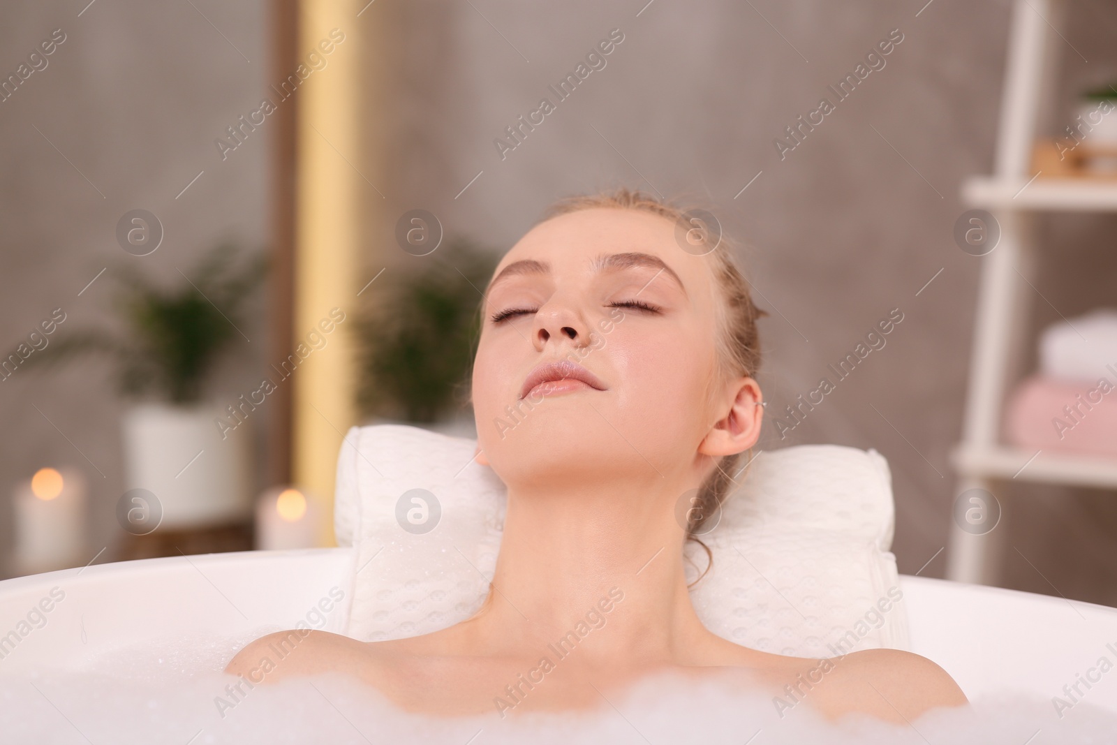 Photo of Young woman using pillow while enjoying bubble bath indoors